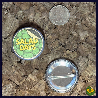 Two buttons on a textured surface, one labeled 'Salad Days' with a coin for scale showing the 1.5" button size.