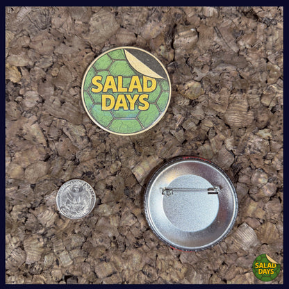 Two buttons on a textured surface, one labeled 'Salad Days' with a coin for scale showing the 2.25" button size.